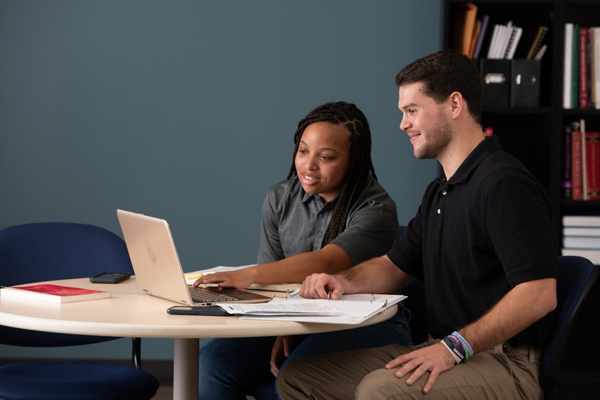 Two students sitting together reviewing study materials on a laptop