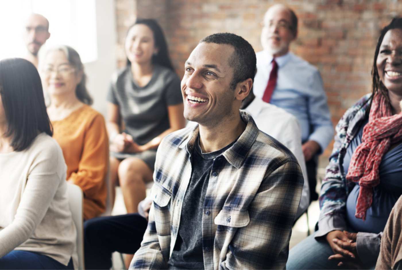 A group of diverse individuals smiling and listening to someone outside of the photo