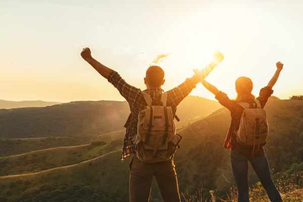 Two individuals on the top of a mountain with their arms raised in celebration