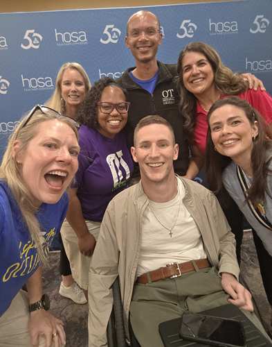 A man in a wheelchair surrounded by six people, all smiling.