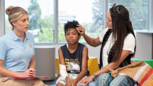 An OTR sits with a mother and her son. The mother is brushing hair from her son's forehead.