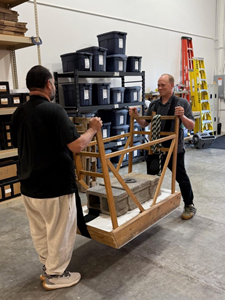Two men lift a wooden structure weighted down with concrete bricks.