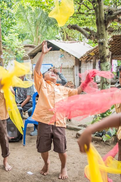 a young child smiling and laughing while throwing colored cloth in the air