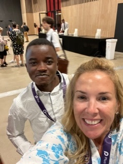 A woman and a man who is slightly behind her pose in a conference hall.