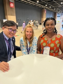 A man and two women pose around a table in a conference hall.