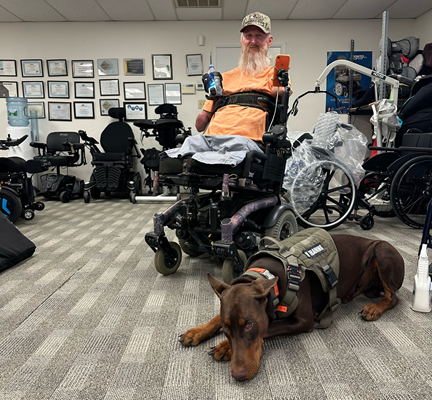 A man in a power wheelchair. His service dog lies next to him.