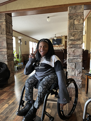 A woman in a wheelchair forms a V gesture with her fingers.