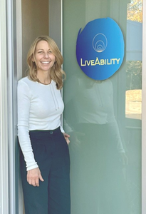 Mac MacEwen stands in front of a door that has the name LiveAbility on it.