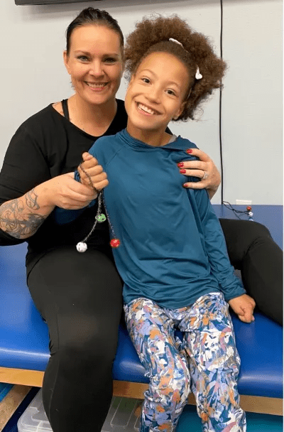 Melanie Thompson poses with a young girl who is holding some jingle bells.