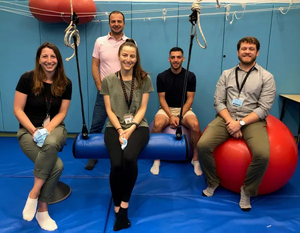 Five OTRs pose with therapy gym equipment.