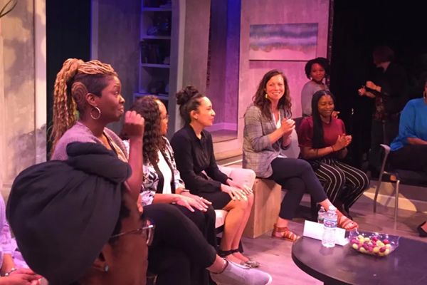 Sally Wasmuth sits with a group of women of color on a stage.
